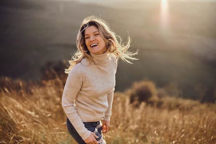 Woman laughing outdoors in a golden field at sunset, with her hair blowing in the wind, representing health and happiness