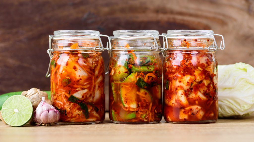 Glass jars of kimchi and fermented vegetables on a wooden surface, illustrating the best foods for gut health