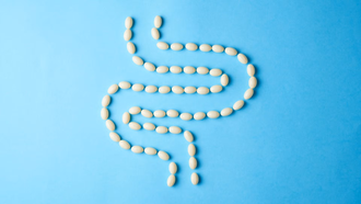 White oval supplement capsules or tablets arranged in the shape of the human intestines (gut) against a light blue background, representing gut health and digestive wellness.